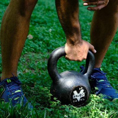 Man training with kettlebell outdoors on grass